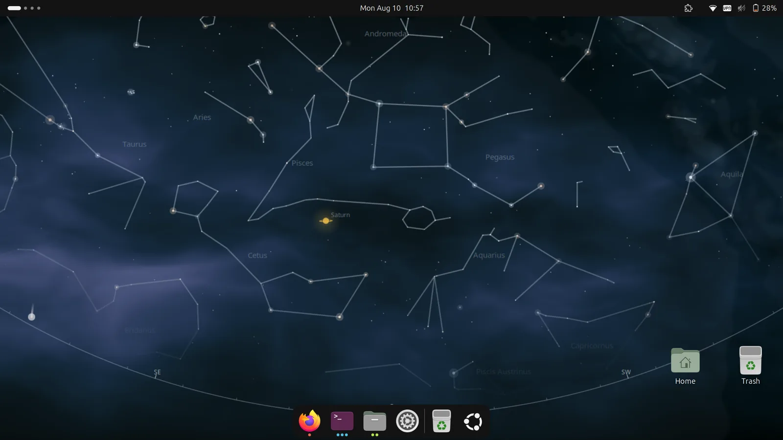 A GNOME desktop whose wallpaper is the computed night sky: constellation
                figures for Pegasus, Aquarius, Aries and Taurus with their names, the Milky
                Way banding across, Saturn labelled and glowing, and the horizon arc marked
                SE and SW. The dock and the Home and Trash icons are in shot.